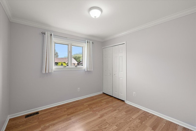 unfurnished bedroom with light wood-style flooring, baseboards, visible vents, ornamental molding, and a closet