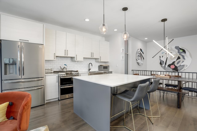 kitchen with appliances with stainless steel finishes, light countertops, a center island, white cabinetry, and dark wood-style floors