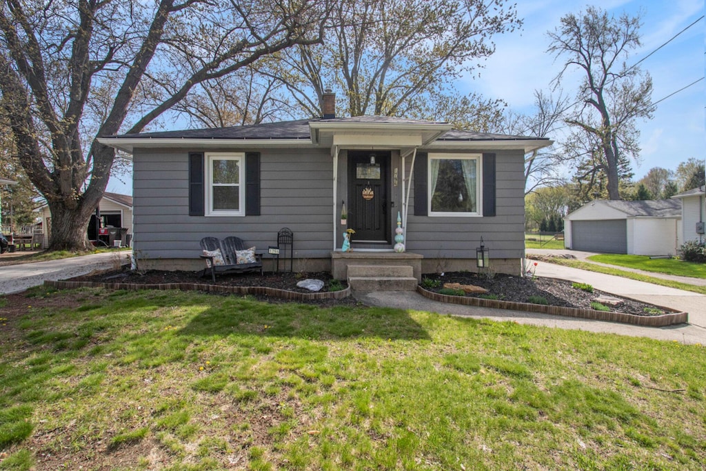bungalow-style home featuring driveway, an outbuilding, a front yard, and a chimney