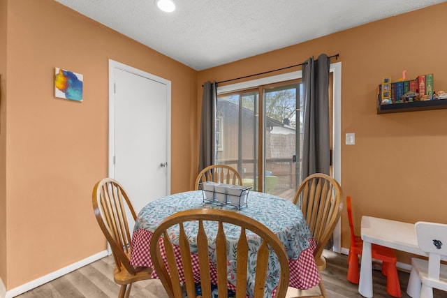 dining space with baseboards, a textured ceiling, and wood finished floors