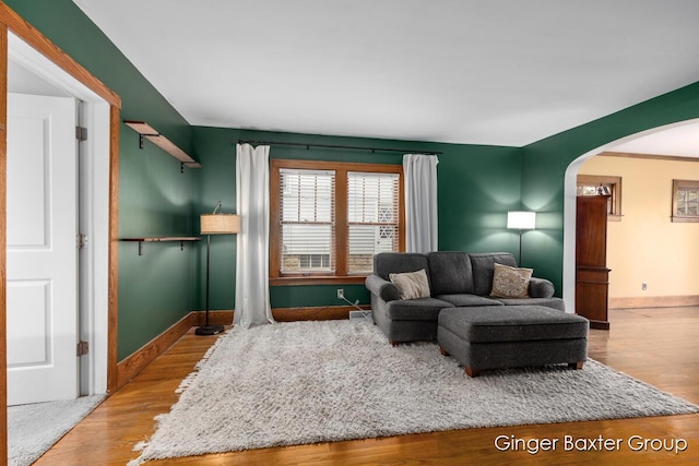 living area with arched walkways, baseboards, and wood finished floors