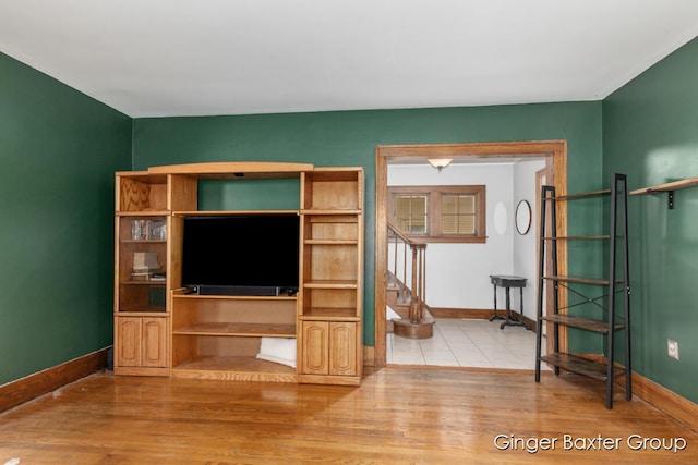 unfurnished living room with stairway, baseboards, and wood finished floors