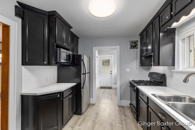 kitchen with a sink, light wood finished floors, dark cabinetry, stainless steel appliances, and tasteful backsplash