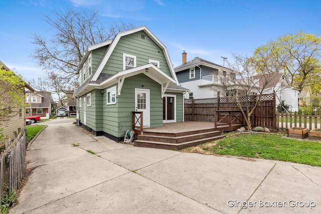 back of property with a gambrel roof, fence, and a wooden deck