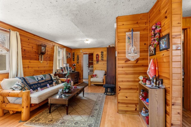 living room featuring light wood-style floors, a textured ceiling, and wooden walls