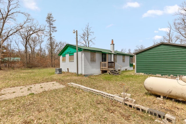 rear view of house with concrete block siding, a chimney, a yard, and central AC