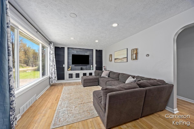 living room with arched walkways, hardwood / wood-style flooring, a textured ceiling, and visible vents