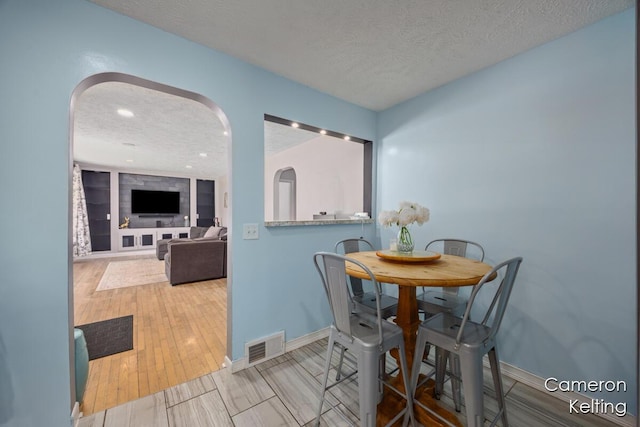dining area featuring a textured ceiling, visible vents, baseboards, and wood finished floors