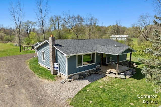 view of front facade featuring a porch, driveway, a chimney, a front yard, and a shingled roof
