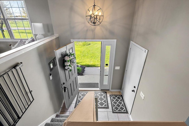 entrance foyer featuring an inviting chandelier, baseboards, tile patterned flooring, and stairway