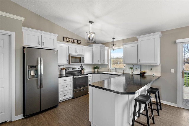 kitchen with dark countertops, appliances with stainless steel finishes, a sink, a peninsula, and white cabinetry