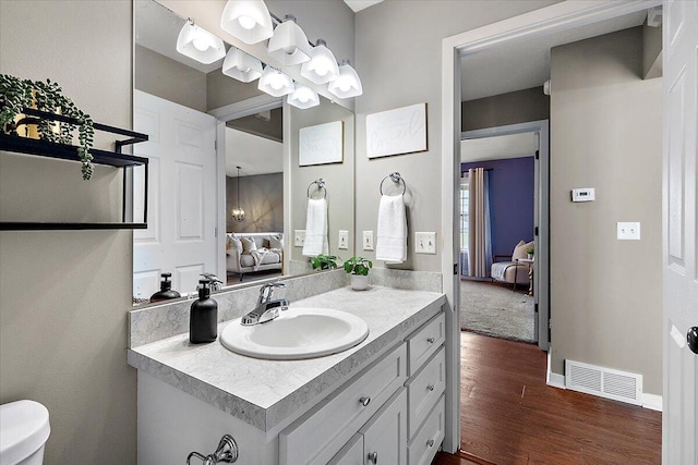 ensuite bathroom featuring visible vents, vanity, wood finished floors, toilet, and ensuite bath