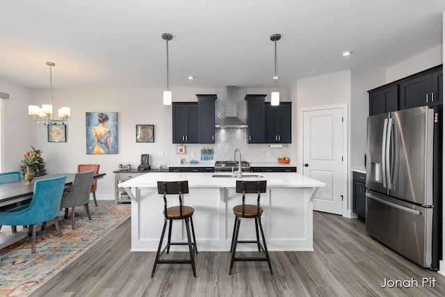 kitchen featuring a sink, light wood finished floors, light countertops, wall chimney exhaust hood, and stainless steel refrigerator with ice dispenser