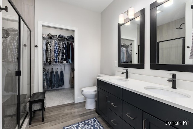 full bathroom with wood finished floors, double vanity, a sink, and a stall shower