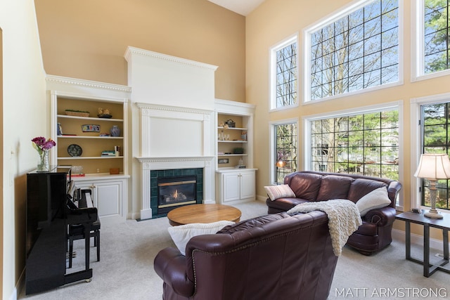 carpeted living area with plenty of natural light, baseboards, a high ceiling, and a tile fireplace