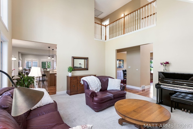 living area featuring visible vents, baseboards, a high ceiling, and light colored carpet