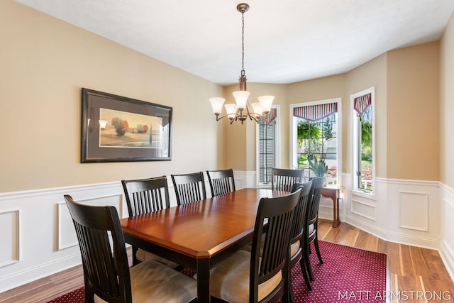 dining space featuring an inviting chandelier, a decorative wall, wood finished floors, and a wainscoted wall