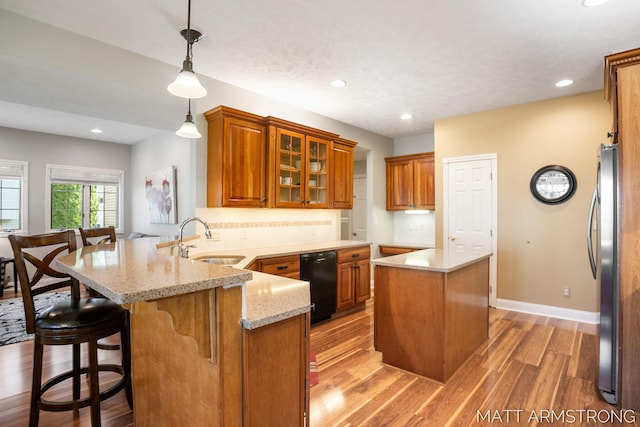 kitchen featuring a sink, light wood-style floors, brown cabinetry, freestanding refrigerator, and a peninsula