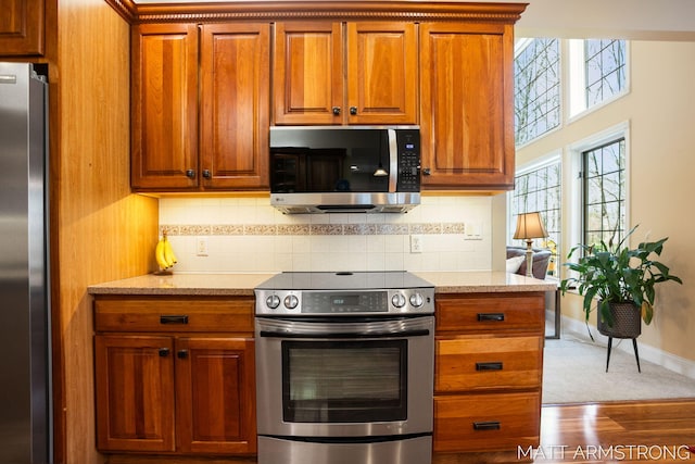 kitchen with brown cabinetry, decorative backsplash, and appliances with stainless steel finishes