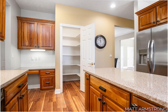 kitchen with brown cabinets, stainless steel refrigerator with ice dispenser, light stone countertops, and wood finished floors