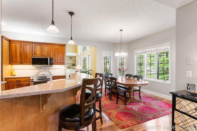kitchen with brown cabinetry, a breakfast bar area, pendant lighting, light stone counters, and stainless steel appliances