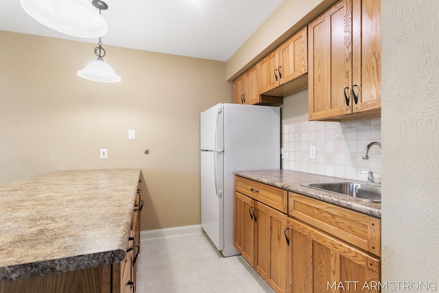kitchen featuring backsplash, pendant lighting, a sink, baseboards, and freestanding refrigerator