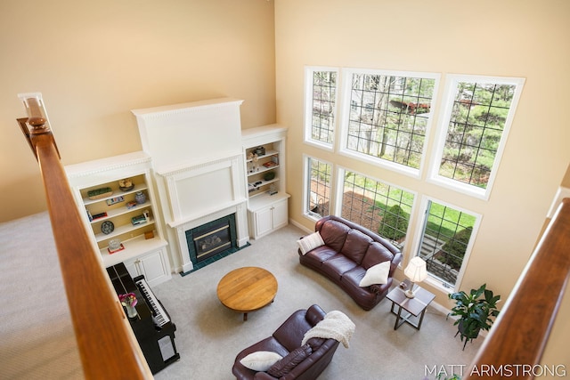 carpeted living room featuring a high ceiling, a fireplace with flush hearth, and built in features