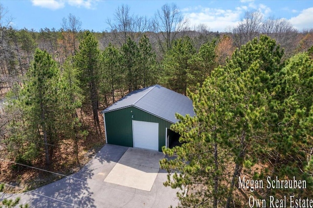 detached garage with a view of trees and concrete driveway