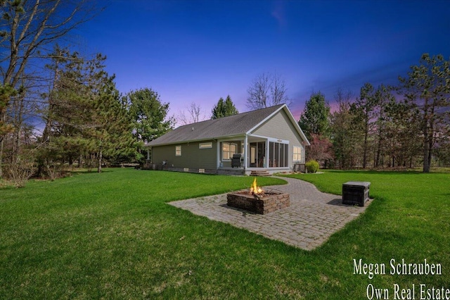 back of property at dusk with a lawn, an outdoor fire pit, and a patio