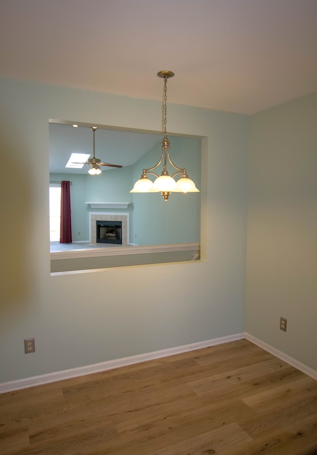 unfurnished room featuring a tiled fireplace, baseboards, a ceiling fan, and wood finished floors