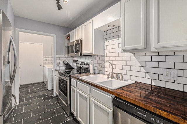 kitchen featuring dark tile patterned floors, decorative backsplash, a sink, stainless steel appliances, and white cabinetry