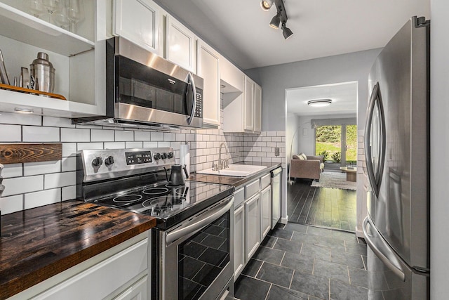 kitchen featuring white cabinets, appliances with stainless steel finishes, a sink, wooden counters, and backsplash