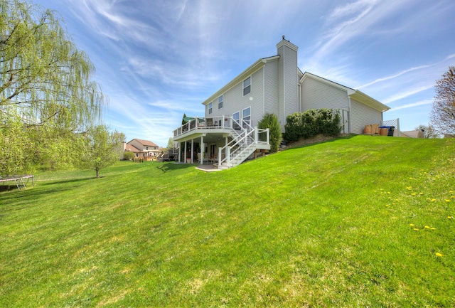 rear view of house with stairs, a trampoline, a lawn, and a deck