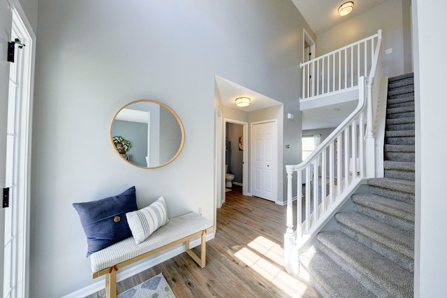 stairway with baseboards, wood finished floors, and a towering ceiling