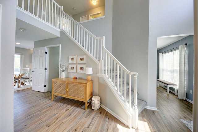 stairway featuring baseboards, a high ceiling, and wood finished floors