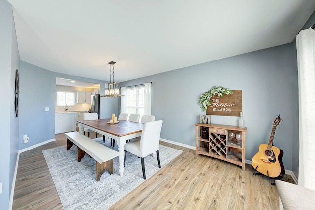 dining area with baseboards, an inviting chandelier, a healthy amount of sunlight, and light wood-style flooring