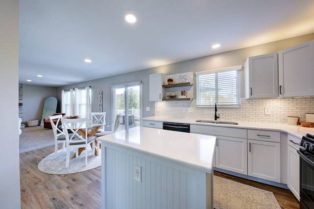 kitchen with a sink, tasteful backsplash, black appliances, and wood finished floors