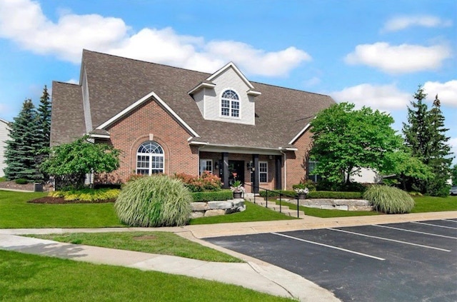 view of front of property with brick siding, uncovered parking, roof with shingles, and a front yard