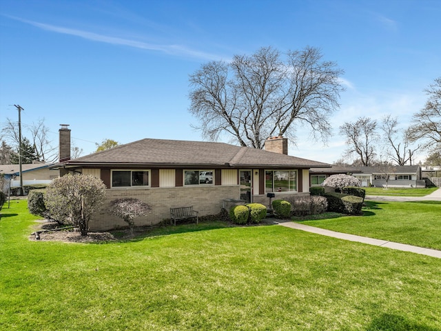 view of front of property with brick siding, a chimney, a shingled roof, and a front yard