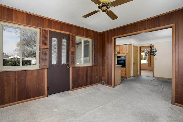 entryway with wood walls, light carpet, a healthy amount of sunlight, and ceiling fan with notable chandelier