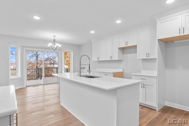 kitchen featuring a sink, white cabinets, light wood finished floors, an inviting chandelier, and an island with sink