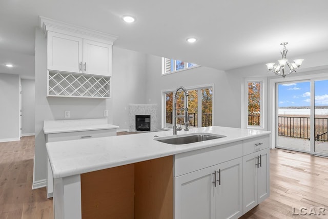 kitchen featuring a high end fireplace, a sink, white cabinets, a chandelier, and light wood-style floors