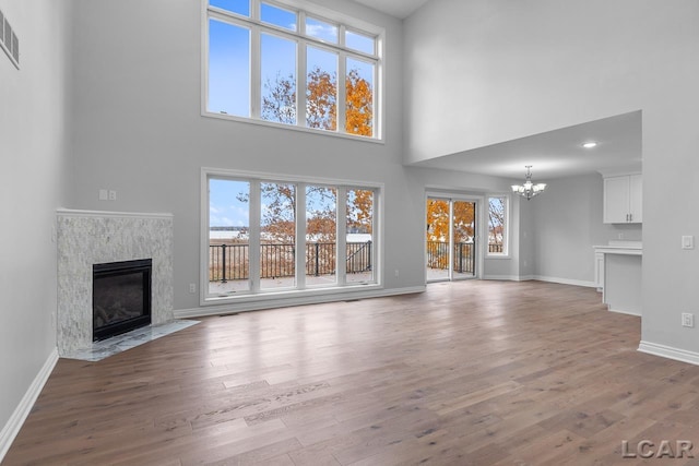 unfurnished living room with a fireplace, a chandelier, baseboards, wood finished floors, and a towering ceiling