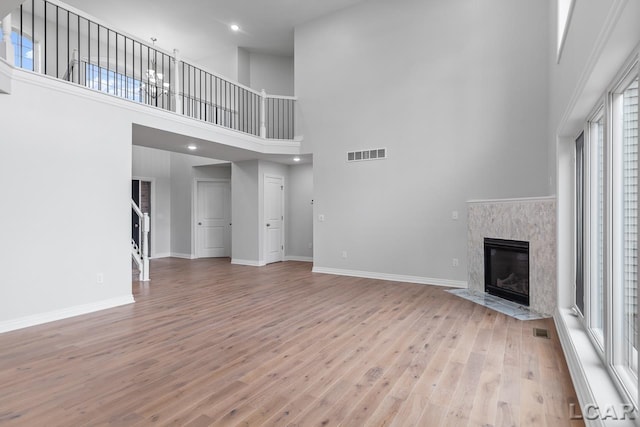 unfurnished living room with a high ceiling, a premium fireplace, light wood-style flooring, baseboards, and visible vents