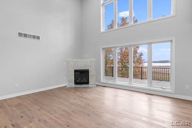 unfurnished living room featuring wood finished floors, visible vents, a healthy amount of sunlight, and a towering ceiling