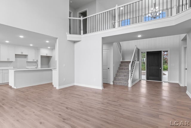 unfurnished living room with stairs, a towering ceiling, baseboards, recessed lighting, and light wood finished floors