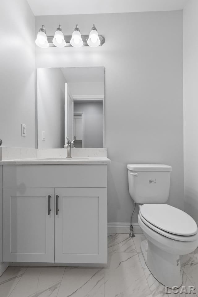 bathroom with toilet, baseboards, marble finish floor, and vanity