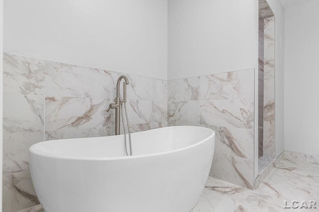 bathroom featuring tile walls, marble finish floor, and a freestanding bath