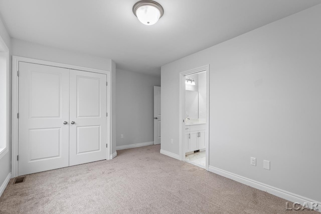 unfurnished bedroom with connected bathroom, baseboards, light carpet, and a closet