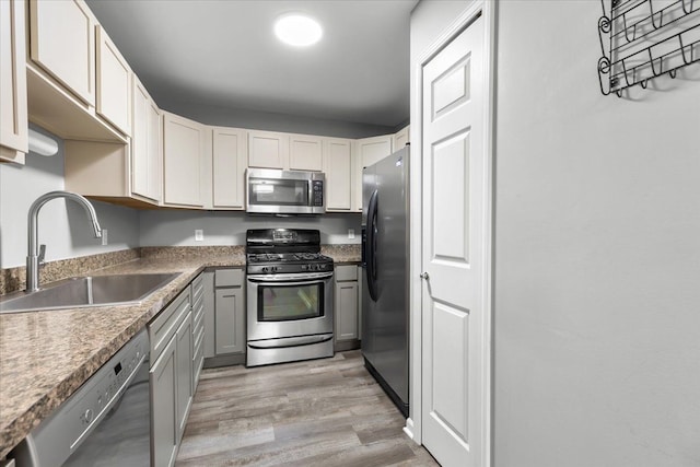 kitchen with stainless steel appliances, gray cabinetry, a sink, and light wood finished floors